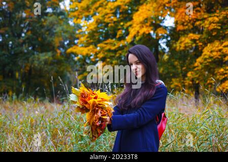 Smiling woman makes an autumn wreath from colorful maple leaves. Outdoor leisure. Fall concept Stock Photo