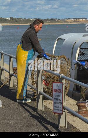 FishermanStanding On The Quayside Unloading Lobster Pots From A Fishing Boat At Mudeford Quay, UK Stock Photo