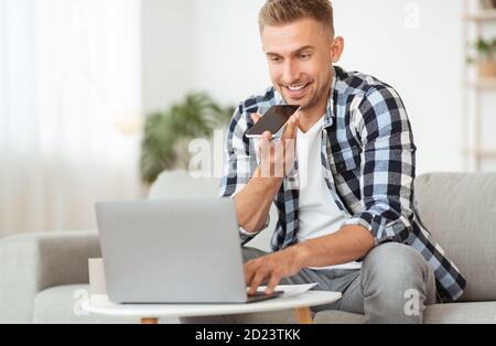 Young man using voice assistant on his cellphone, using pc Stock Photo