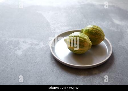 Two variegated pink lemons with green-striped rind in grey plate on concrete background with copy space Stock Photo