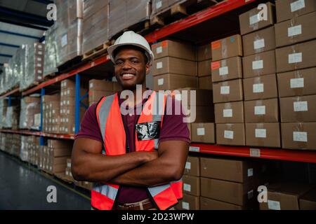 Smiling mixed race worker standing besides parcels in warehouse. Stock Photo
