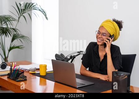 Shot of young latin woman working at home office with laptop speaking on mobile phone Stock Photo