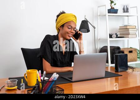 Shot of young latin woman working at home office with laptop speaking on mobile phone Stock Photo