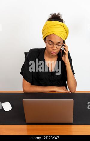 Shot of young latin woman working at home office with laptop speaking on mobile phone Stock Photo