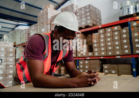 Mixed race male browsing on cellular device chatting to colleagues standing in warehouse Stock Photo