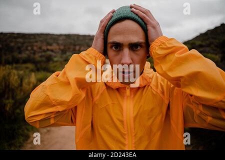 Portrait of attractive young male athlete adjusting hat before running on outdoor mountain path in cloudy weather Stock Photo
