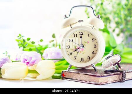 Retro alarm clock, notebook and spring flowers. Stock Photo