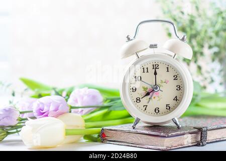 Retro alarm clock, notebook and spring flowers. Stock Photo