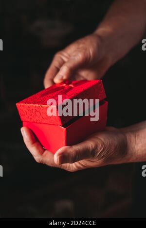 Close-up of elderly female hands opening red gift box. Black, dark background Stock Photo