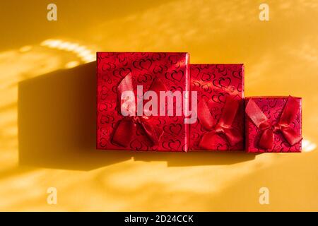 Three red gift boxes in different sizes isolated on yellow background Stock Photo