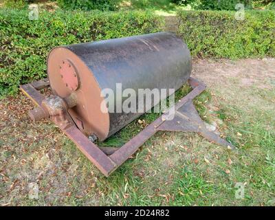 Steel old grass roller on grass yard. Lawn Roller for levelling uneven turf. Selective focus. Stock Photo