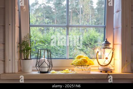 Autumn bouquet of yellow roses on the windowsill, candles, flowers, lantern. Scandinavian style. White window with mosquito net in rustic wooden house Stock Photo