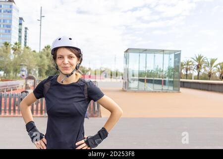 Young happy roller skater caucasian woman in the white helmet and black sporty clothes on a sunny day in the skatepark, urban environment Stock Photo