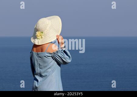 Woman in sun hat and blue dress standing on a sea background. Beach vacation, relax and dreaming concept Stock Photo