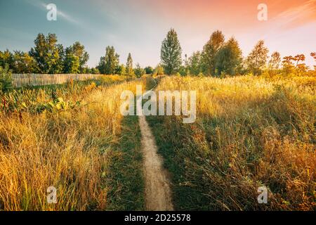 Landscape Of Rural Country Path Through Field With Dry Grass In Early Autumn Season. Pathway, Way, Path, Road At Sunset Sunrise. Agricultural Rural Stock Photo