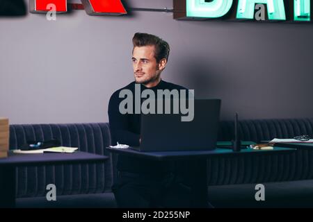 Young businessman sitting at a desk in a shared office space looking deep in thought and working on a laptop Stock Photo