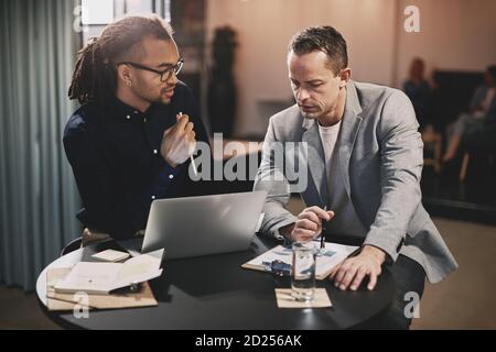 Two diverse businessmen talking together over a laptop while working at a table in an office Stock Photo