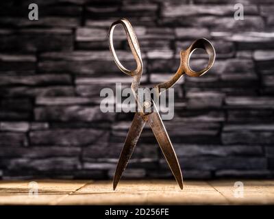 Rusty vintage pair of scissors balance on timber flooring against slate background Stock Photo