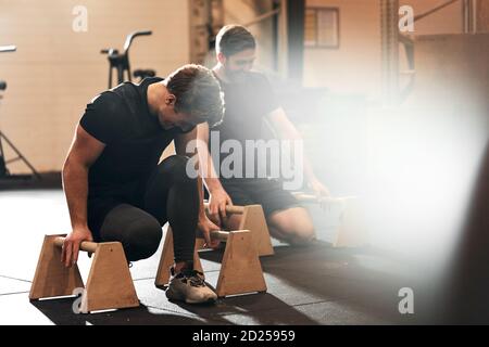 Two fit young men in sportswear getting ready for a workout on parallettes on the floor of a gym Stock Photo