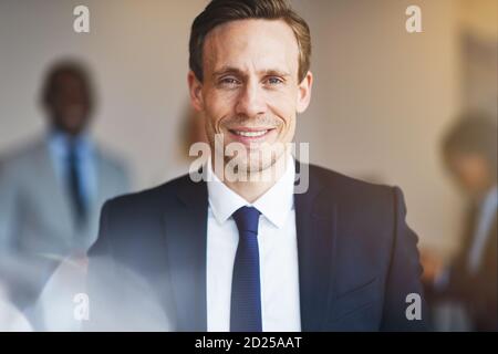 Confident young businessman standing in an office with a diverse group of colleagues standing in the background Stock Photo