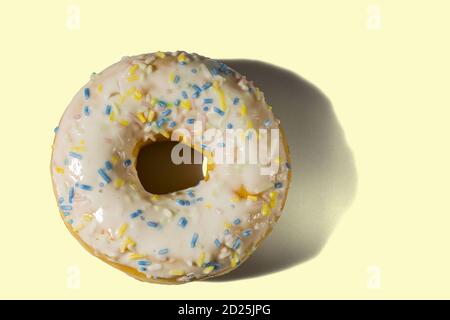 View of donut sprinkled with multicolored glaze isolated on yellow background. Food and drink concept. Stock Photo
