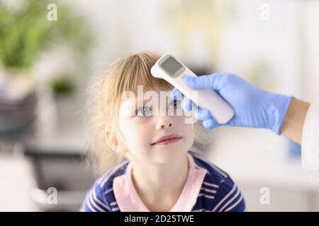 Pediatrician doctor in rubber glove measures temperature of child with infrared thermometer portrait Stock Photo