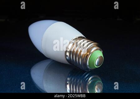 The Electric light bulb on table with reflection on black background. Instrument for illumination of the room Stock Photo