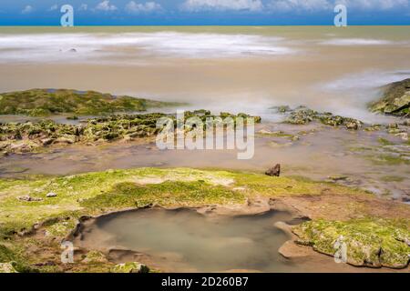 Blurred ocean over reefs with algae and under blue sky charged with nimbus clouds. Stock Photo