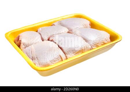 Raw and uncooked chicken thighs in a yellow plastic container. Meat of poultry in tray, isolated on white background Stock Photo