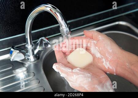 a young guy washes his hands with soap under the faucet over a metal sink on a black dark background. Virus prevention. Hygienic procedure. Wash your Stock Photo