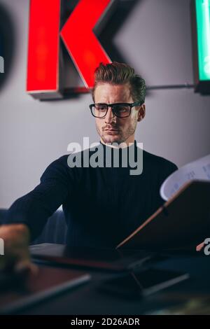 Young businessman sitting at a desk in a modern office going over paperwork on a clipboard and working on a laptop Stock Photo