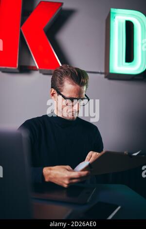 Young businessman going over documents on a clipboard while sitting at his desk in a modern office Stock Photo