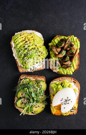 Assortment of avocado toasts on black background. Avocado toast with egg, cucumber, fried mushrooms and seeds Stock Photo