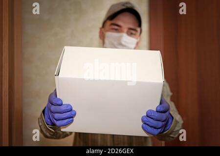 Concept of delivery goods during quarantine 2019-ncov. Young man in medical mask and blue gloves holds cardboard box in hands. Contactless delivery Stock Photo