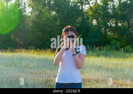 Young woman with camera lens. A beautiful brunette photographer is taking pictures in nature on a summer day. Stock Photo