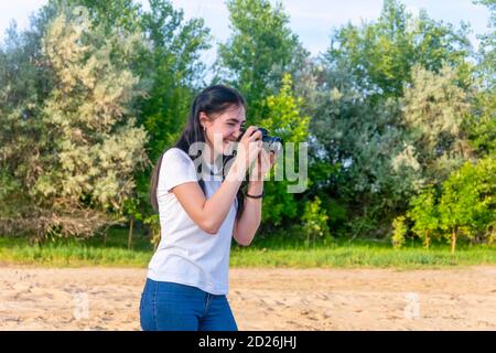 Professional photographer woman at work. Taking pictures outdoors in the park. The brunette looks at the camera and laughs. selective focus. Stock Photo