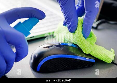 woman disinfects the computer mouse with a disinfectant liquid. Disinfection of premises. Cleaning of the workplace in the office. Disinfection of per Stock Photo