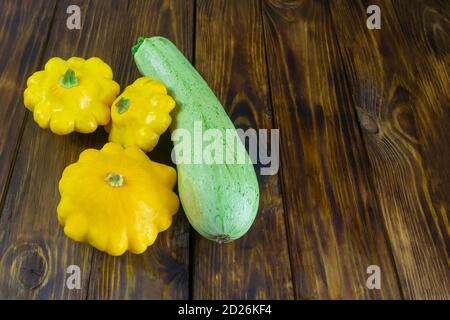 Small yellow squash and long green squash on a wooden table. Autumn harvest of vegetables. Copy space. Stock Photo