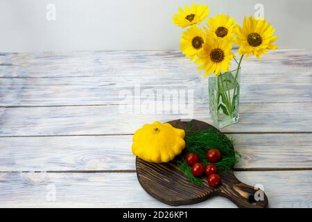 Yellow flowers in glass vase on wooden table with colorful vegetables. Harvest healthy foods. Stock Photo