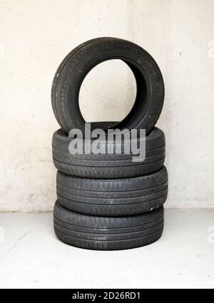 Stack of four old used vehicle tyres in a garage or workshop with the top tyre balancing upended on the others against a wall with copy space below Stock Photo