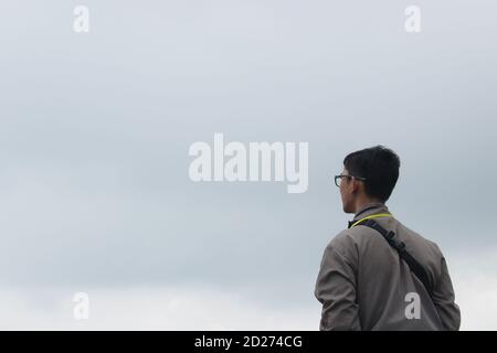 a portrait of an Asian man with glasses looking at the cloudy sky