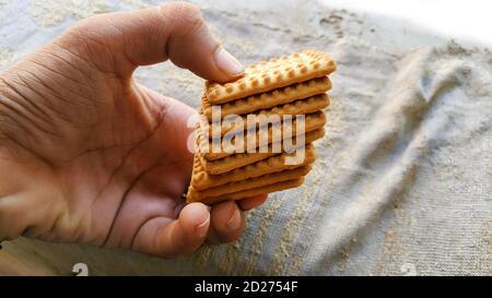 Man holding many biscuits in hand. Many Brown wheat biscuits with tea isolated on white background Stock Photo