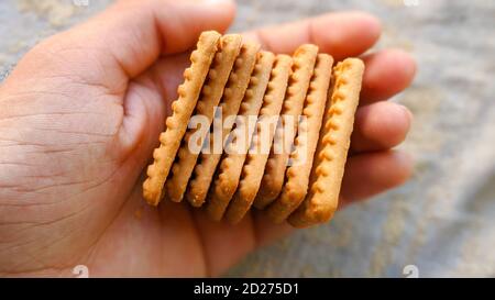 Man holding many biscuits in hand. Many Brown wheat biscuits with tea isolated on white background Stock Photo