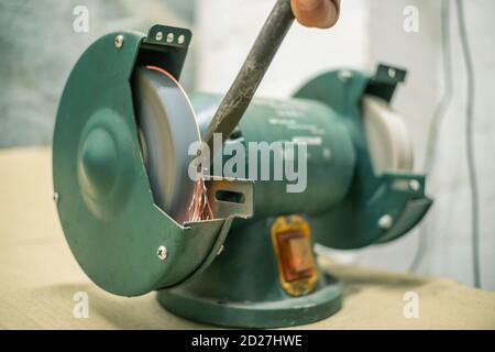 master sharpens a chisel on a grinding machine Stock Photo