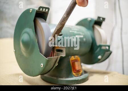 master sharpens a chisel on a grinding machine Stock Photo