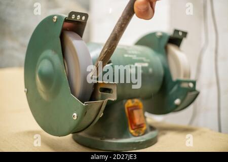 master sharpens a chisel on a grinding machine Stock Photo