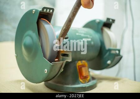 master sharpens a chisel on a grinding machine Stock Photo