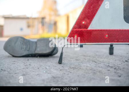 An accident on the road involving a person. Close up of a man's boot and an emergency stop sign Red triangle Stock Photo
