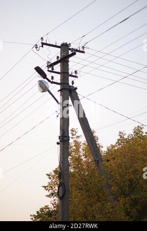 old stone pillar with wires near autumn tree on the white sky background. Stock Photo