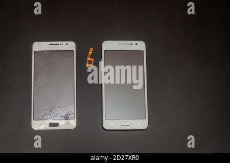 Smartphone after repairing a cracked touch screen. Nearby is a cracked touch screen. Black background with copy space. Stock Photo